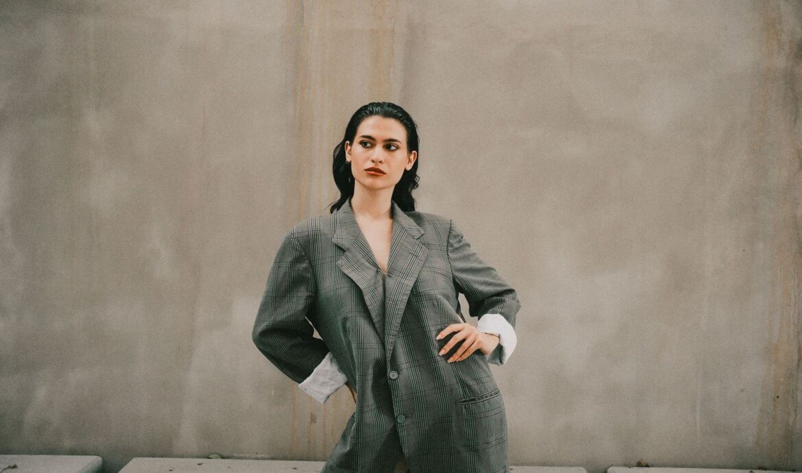 Person i oversized, randig blazer med markerad siluett mot neutral vägg